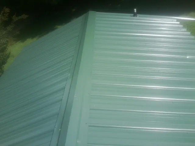 New green metal panels meeting at the ridge of a roof — Flat Roof Repair work by our crew in Riverdale